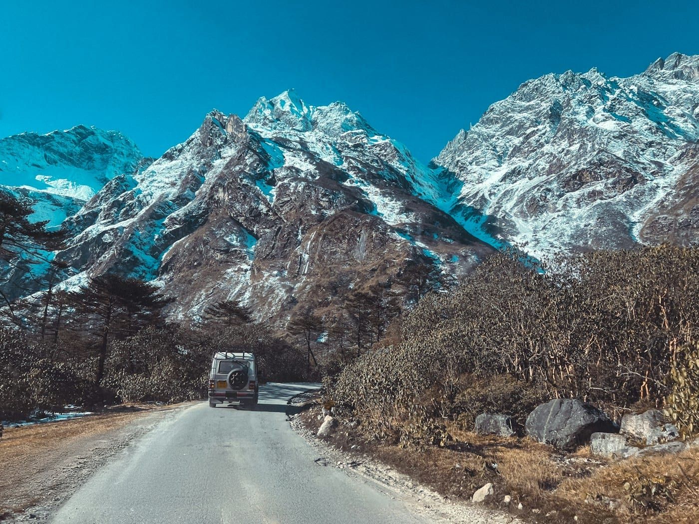Vehicle on a mountain road below snowy peaks